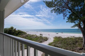 A beach view from a balcony with a railing, clear sky, and a few people on the sand.