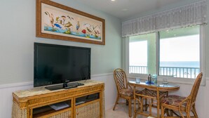 Una sala de estar con televisión de pantalla plana, muebles de mimbre, un cuadro y vista a la playa.