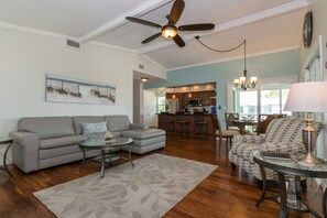Un salon spacieux avec un canapé gris, un tapis à motifs et un ventilateur de plafond.