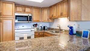 Una cocina con armarios de madera, encimera de granito, microondas, estufa, fregadero y cafetera.