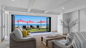 A modern living room with wicker furniture, a coffee table, and a view of the ocean through large glass doors. - Single Family Beachfront Home, Private Beach P1735-0 (Oceanside)
