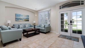 A living room with two light blue sofas, a dark wooden coffee table, and a painting on the wall. - June Court | Waterfront 4BR w/ Pool, Dock, Open Layout & Near Beach (Marco Island)