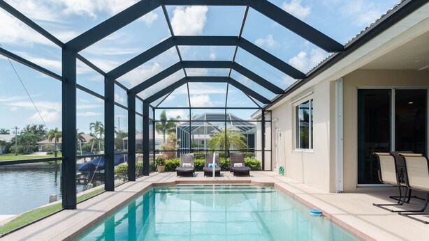 A swimming pool with a glass enclosure, lounge chairs, and a view of a residential area. - June Court | Waterfront 4BR w/ Pool, Dock, Open Layout & Near Beach (Marco Island)