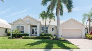 A single-story house with a garage, a front lawn, and palm trees. - June Court | Waterfront 4BR w/ Pool, Dock, Open Layout & Near Beach (Marco Island)