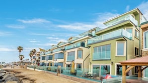 A row of modern beachfront condominiums with balconies, a sandy beach, and palm trees. - Ultimate Serene Escape P819-6 (Oceanside)