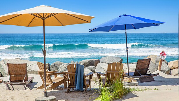 A beach with two wooden chairs and two beach umbrellas, one yellow and one blue, overlooking the ocean. - Pet Friendly Oceanfront Unit in Oceanside P1315-2 (Oceanside)