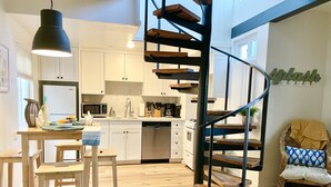 A modern kitchen with white cabinets, a wooden dining table, and a spiral staircase.