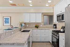 A modern kitchen with white cabinets, a granite countertop, a stainless steel stove, and a microwave.