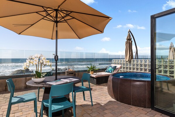 Ein Balkon mit Meerblick, ein Tisch mit Stühlen, ein großer Sonnenschirm und eine Whirlpool-Badewanne.