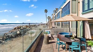 Eine Terrasse am Meer mit einem runden Tisch, Stühlen, einem Mülleimer und Blick auf den Ozean.