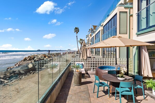 A seaside patio with a round table and chairs, a trash can, and a view of the ocean.
