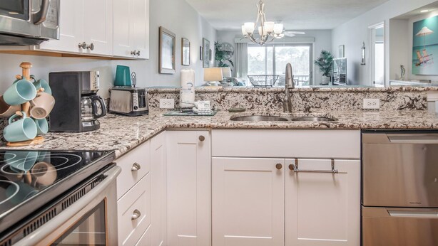 A modern kitchen with white cabinets, a granite countertop, stainless steel appliances, and a view to the dining area.