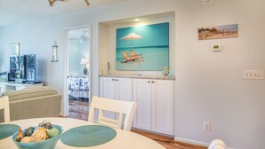 A dining area with a table set for four, a chandelier, and a painting of a beach scene above the table.