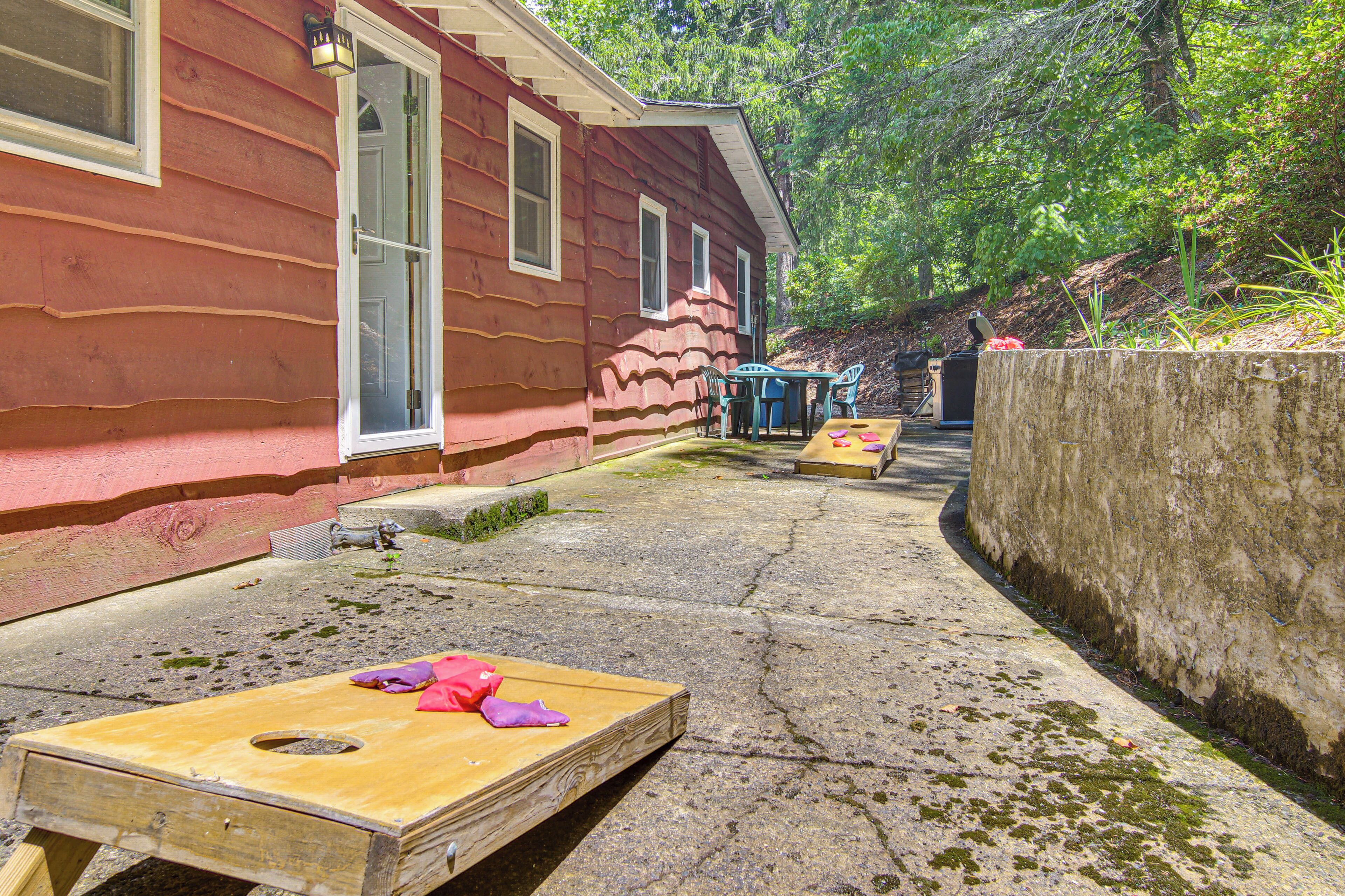 A wooden deck with two wooden tables and chairs, a concrete pathway, and a red house with windows and a door.