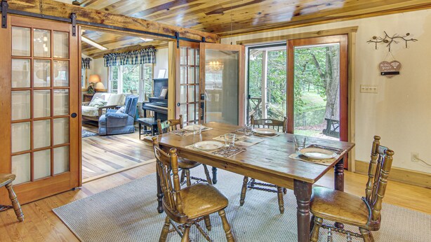A wooden dining table with chairs, a sliding glass door, and a view of the outdoors. - 20-Acre Cabin w/ Pond: 5 Mi to Biltmore Estate! (Asheville)