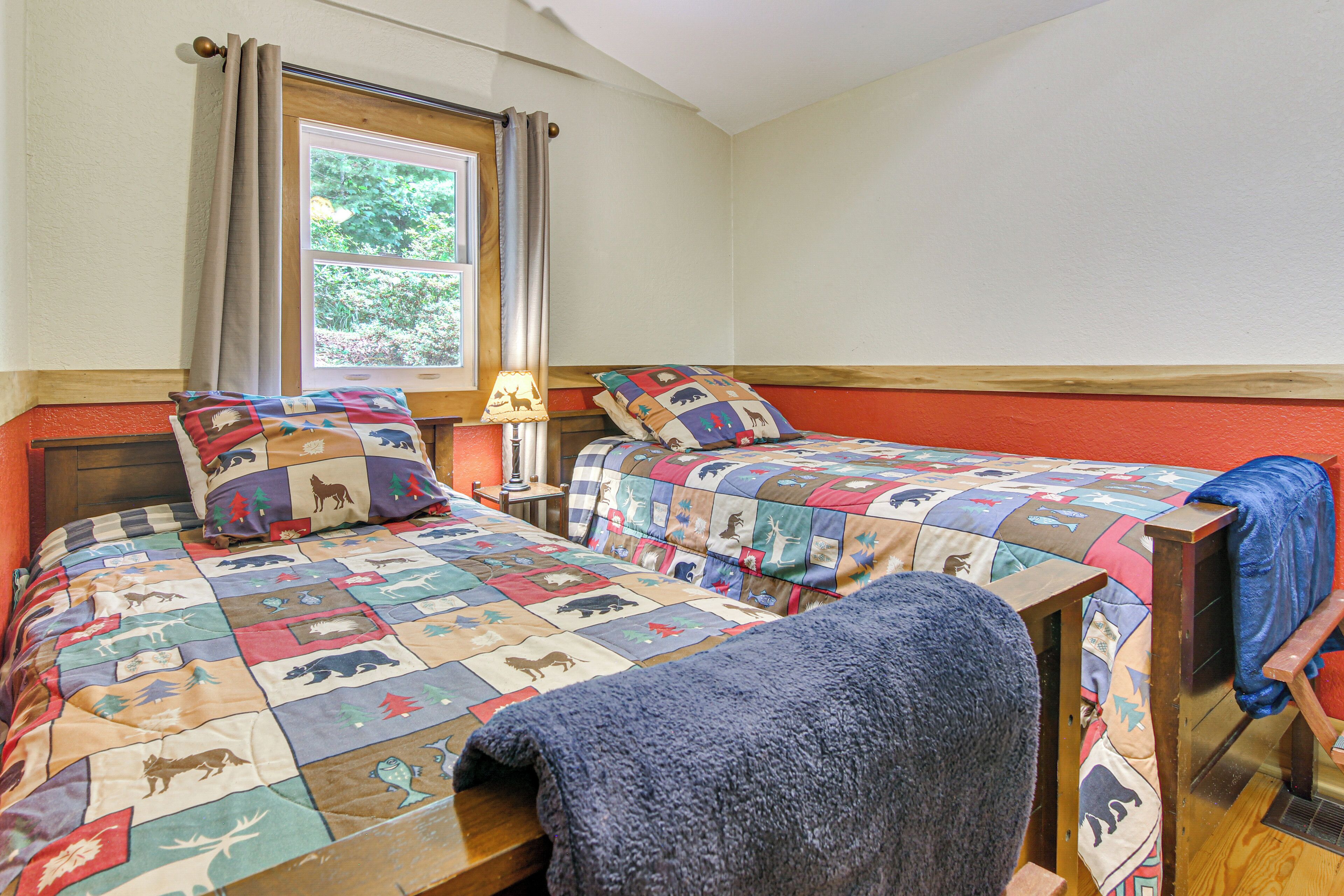 A bedroom with two beds, each with a quilted bedspread featuring animal prints, a window with curtains, and a nightstand with a lamp.