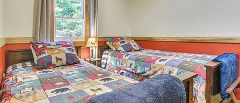 A bedroom with two beds, each with a quilted bedspread featuring animal prints, a window with curtains, and a nightstand with a lamp.
