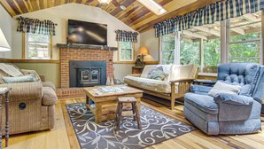 A cozy living room with a fireplace, wooden ceiling, and large windows. - 20-Acre Cabin w/ Pond: 5 Mi to Biltmore Estate! (Asheville)