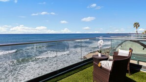A balcony with a glass railing overlooking the ocean, featuring wicker furniture and a small potted plant. - Spacious Beachfront Family Retreat - 819-4 (Oceanside)