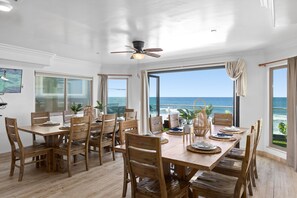 Un espace repas avec vue sur l’océan, des meubles en bois et un ventilateur de plafond.