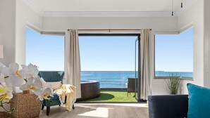 A spacious room with a large window overlooking the sea, a comfortable seating area with a sofa and armchair, and a small side table with a vase of flowers. - Spacious Beachfront Family Retreat - 819-4 (Oceanside)