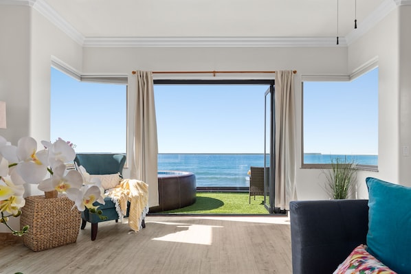 Une pièce spacieuse dotée d’une grande fenêtre donnant sur la mer, d’un coin salon confortable avec un canapé et un fauteuil, ainsi qu’une petite table d’appoint sur laquelle est posé un vase de fleurs.