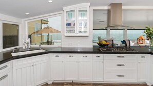 Cozinha moderna com armários brancos, bancada preta e uma grande janela com vista para o oceano.