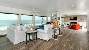 Uma sala de estar ampla com uma grande janela com vista para o oceano, mobiliário branco e uma lareira.