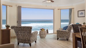 Quarto com vista para o oceano, com duas poltronas estampadas, uma mesinha redonda com frutas e um ventilador de teto.