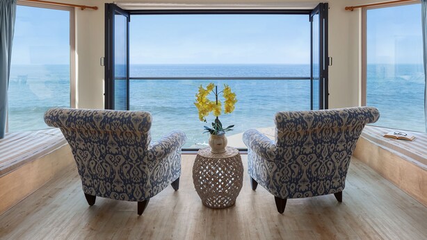 Um quarto com duas poltronas estampadas voltadas para uma grande janela com vista para o mar.