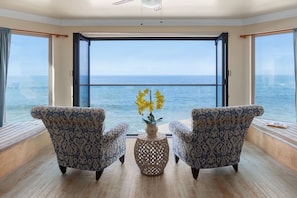 Ein Zimmer mit zwei gemusterten Sesseln, die zu einem großen Fenster mit Meerblick ausgerichtet sind.