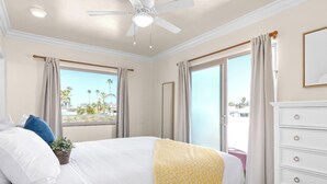 Un dormitorio con cama, ventilador de techo, ventana con cortinas y vista a palmeras.