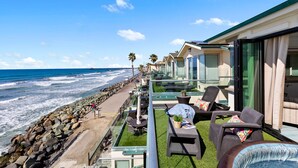 Un balcón con mobiliario exterior, vista al océano y una hilera de casas de playa.