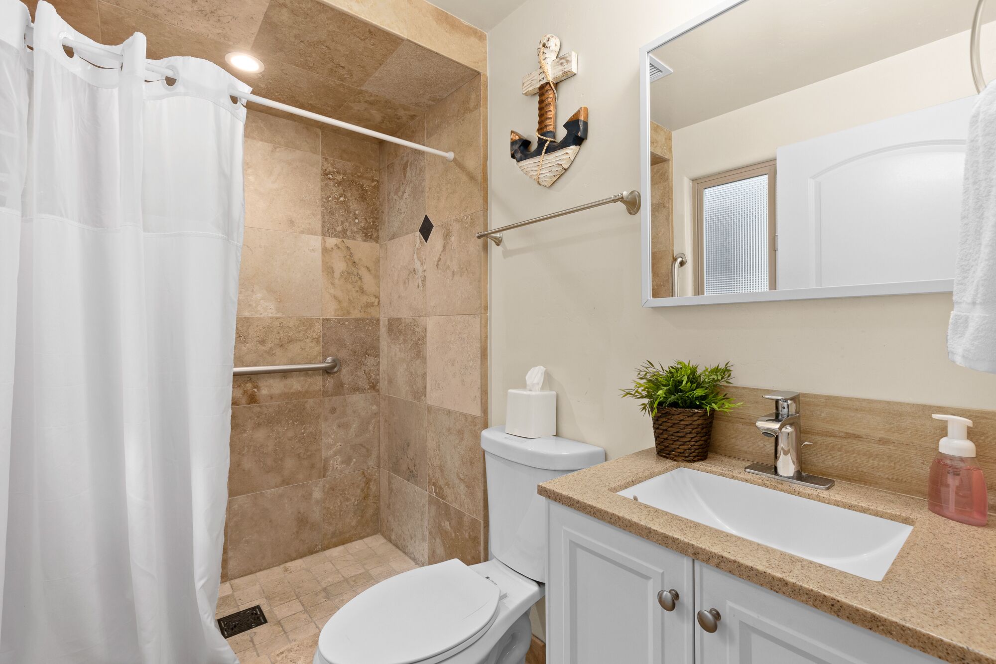 Een badkamer met douche, toilet, wastafel en een decoratief anker aan de muur.