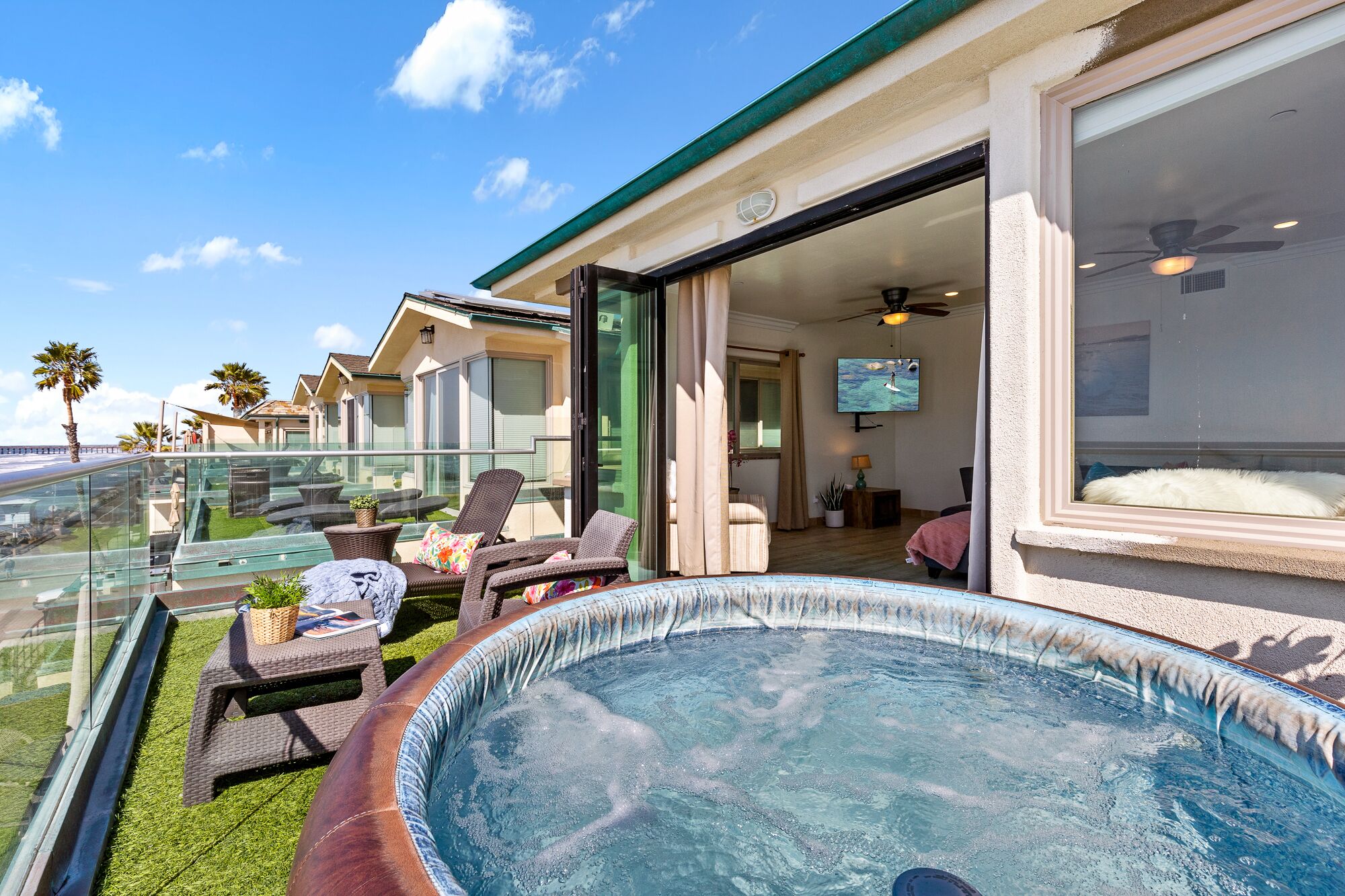 Zwembadgedeelte met ligbedden en een jacuzzi, met uitzicht op een woongebied met huizen en palmbomen.