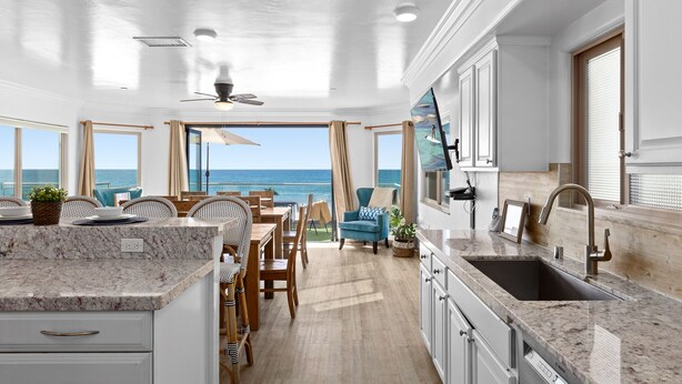 Una cocina moderna con una isla grande, un comedor con vistas al océano y un ventilador de techo.