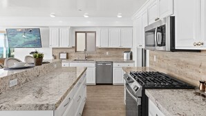 Una cocina moderna con gabinetes blancos, encimeras de granito, electrodomésticos de acero inoxidable y una isla grande con asientos.