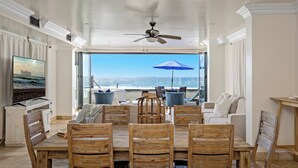 A dining area with a view of the ocean, a ceiling fan, and a large TV screen. - Top Notch Coastal Getaway P813-2 (Oceanside)