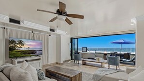 A spacious living room with a large TV, comfortable seating, a ceiling fan, and a view of the ocean. - Top Notch Coastal Getaway P813-2 (Oceanside)