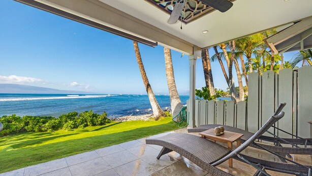 Un espace extérieur moderne avec des sièges, offrant une vue sur l’océan, une terrasse avec un sol carrelé et un ventilateur de plafond.