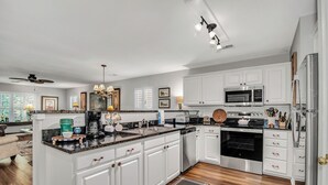 Una cocina moderna con armarios blancos, una isla central, electrodomésticos de acero inoxidable y un ventilador de techo.
