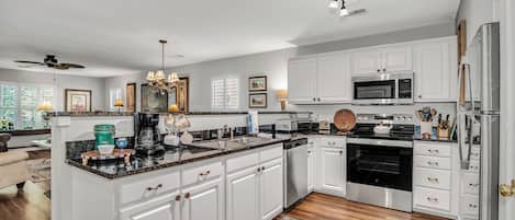 A modern kitchen with white cabinetry, a central island, stainless steel appliances, and a ceiling fan.