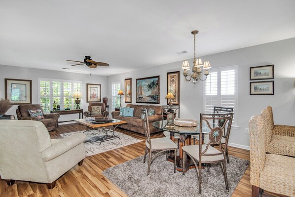 A spacious living room with a ceiling fan, a dining area with a glass table, and a cozy seating arrangement.