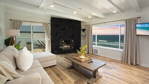 A modern living room with a stone fireplace, a large window with a view of the ocean, and a cozy seating area. - Cozy Beachfront Retreat with Private Spa - 1315-1 (Oceanside)