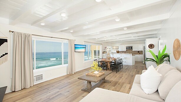 A spacious living area with a large window overlooking the ocean, a dining table, and a cozy seating area. - Cozy Beachfront Retreat with Private Spa - 1315-1 (Oceanside)