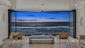 Amplia habitación con un amplio ventanal que ofrece vistas al mar al atardecer.
