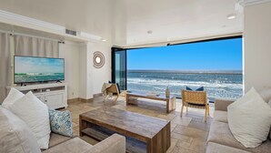 Una sala de estar con un televisor grande, una mesa de centro y asientos orientados hacia una ventana grande con vistas al océano.