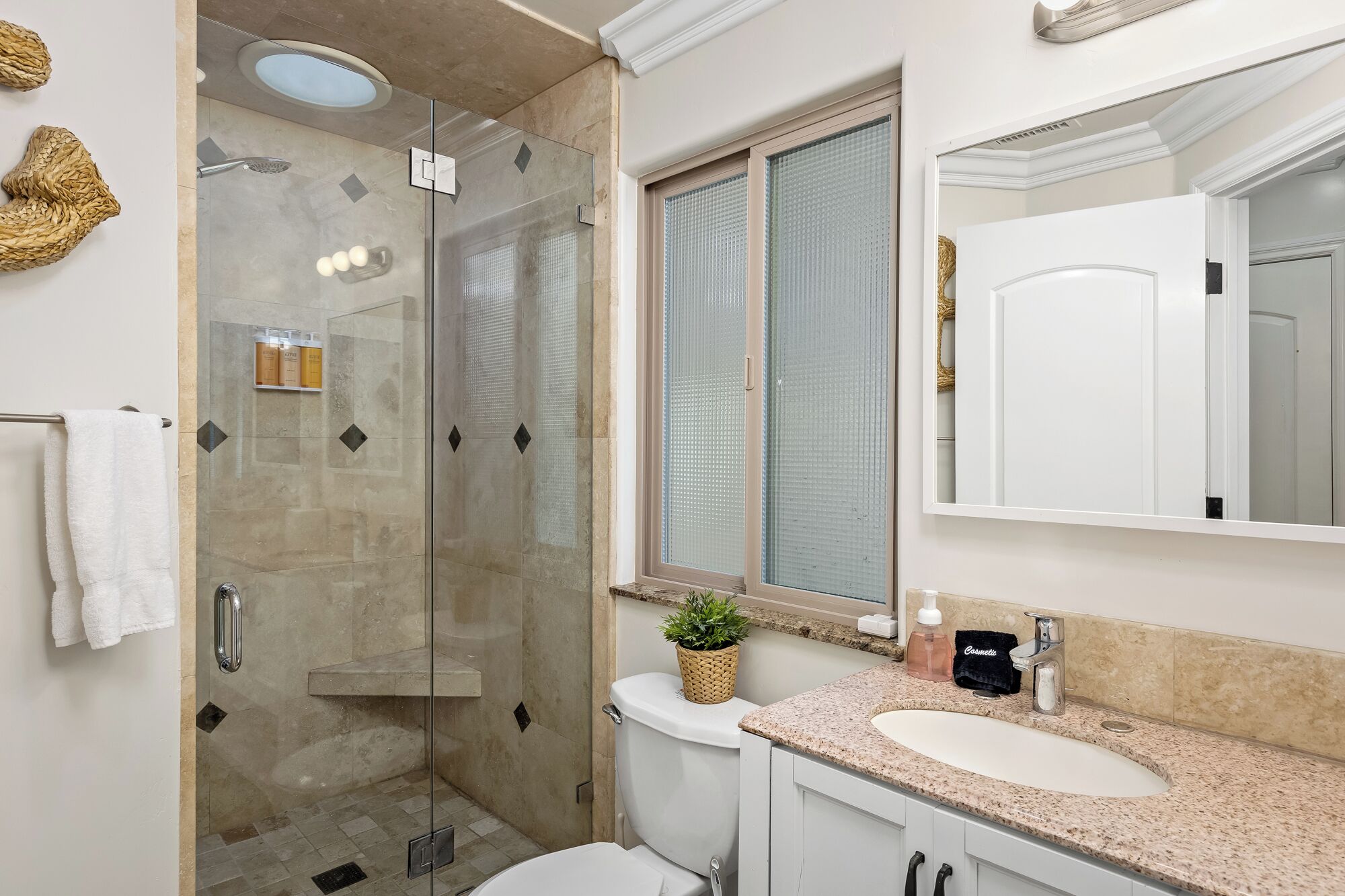 Un baño moderno con ducha de vidrio, inodoro blanco, lavamanos con encimera de granito y un espejo grande.