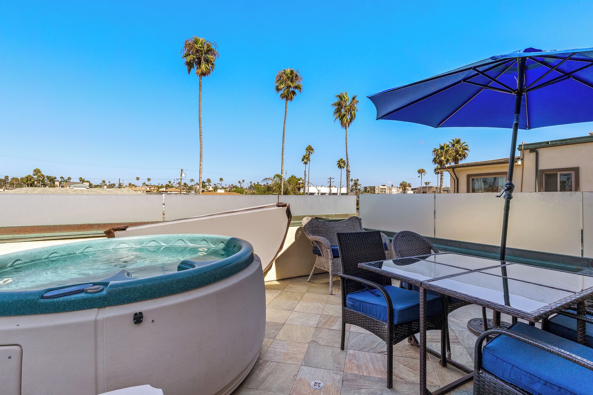 Terraza en la azotea con jacuzzi, sillas de mimbre y una mesa con sombrilla.