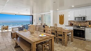 Un comedor amplio con vistas al océano, una cocina con armarios blancos y electrodomésticos de acero inoxidable, y una zona de estar acogedora con un ventanal grande.